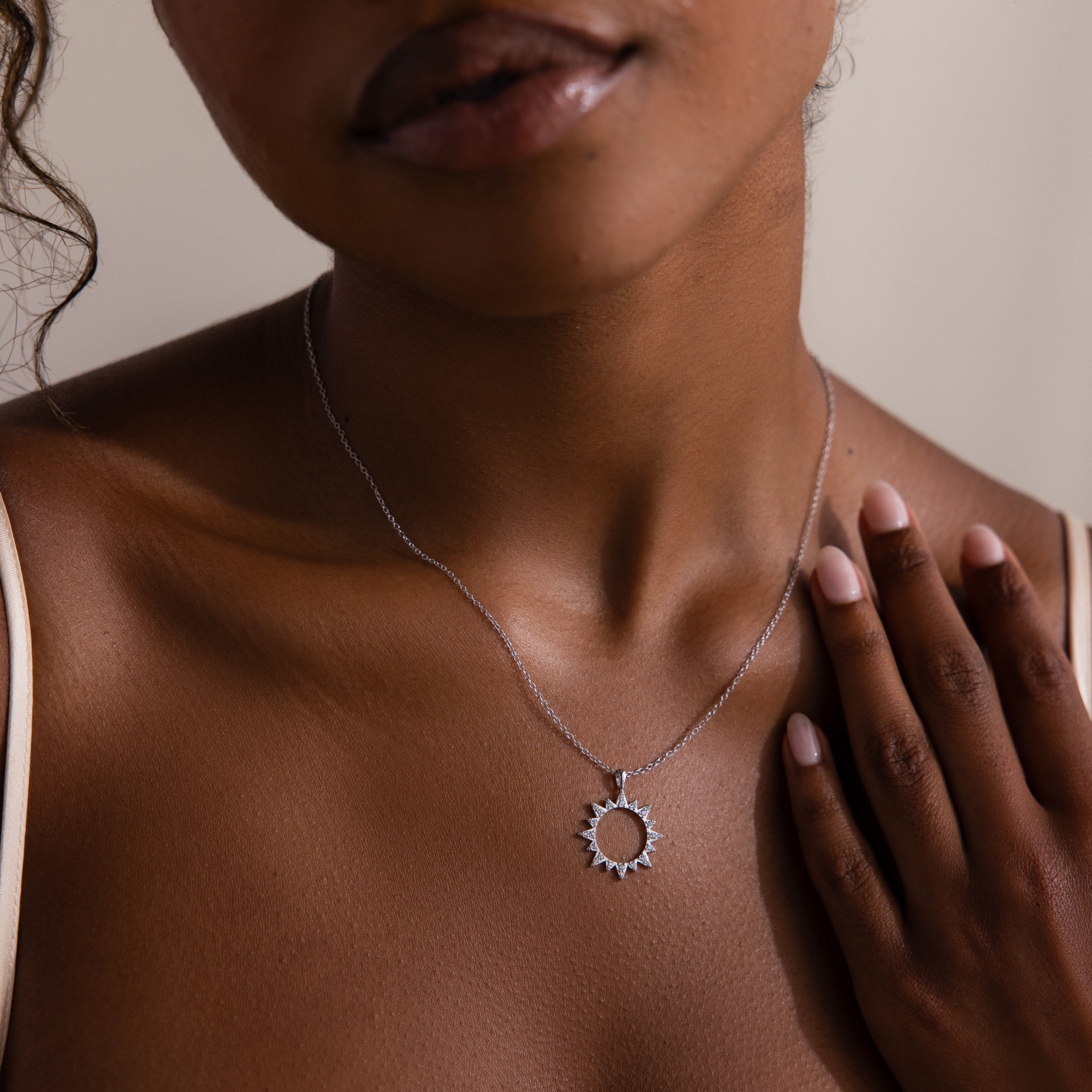 A woman wearing the Pave Sun Necklace in Silver, embellished with sparkling pave accents, gently touches her collarbone.