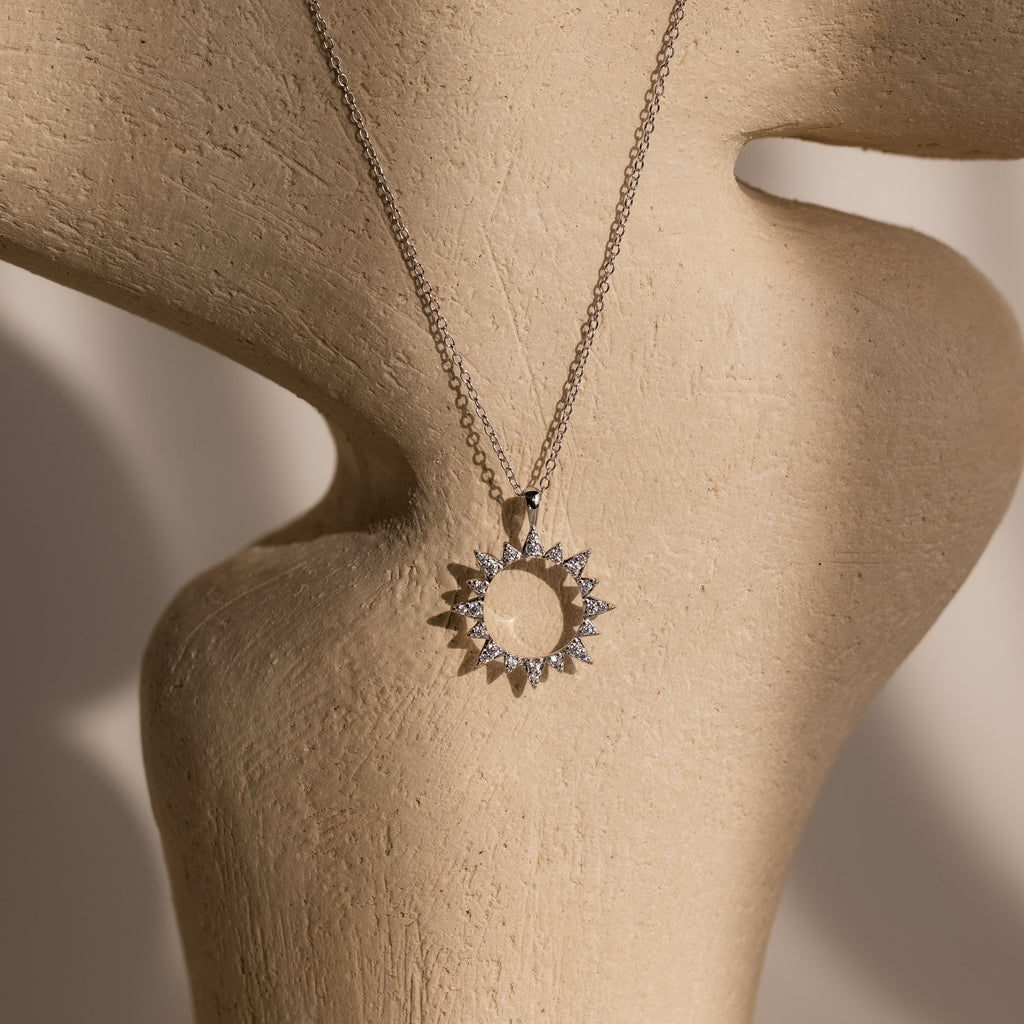 The Pave Sun Necklace in Silver, featuring sparkling pave accents, is displayed on a beige textured mannequin bust.