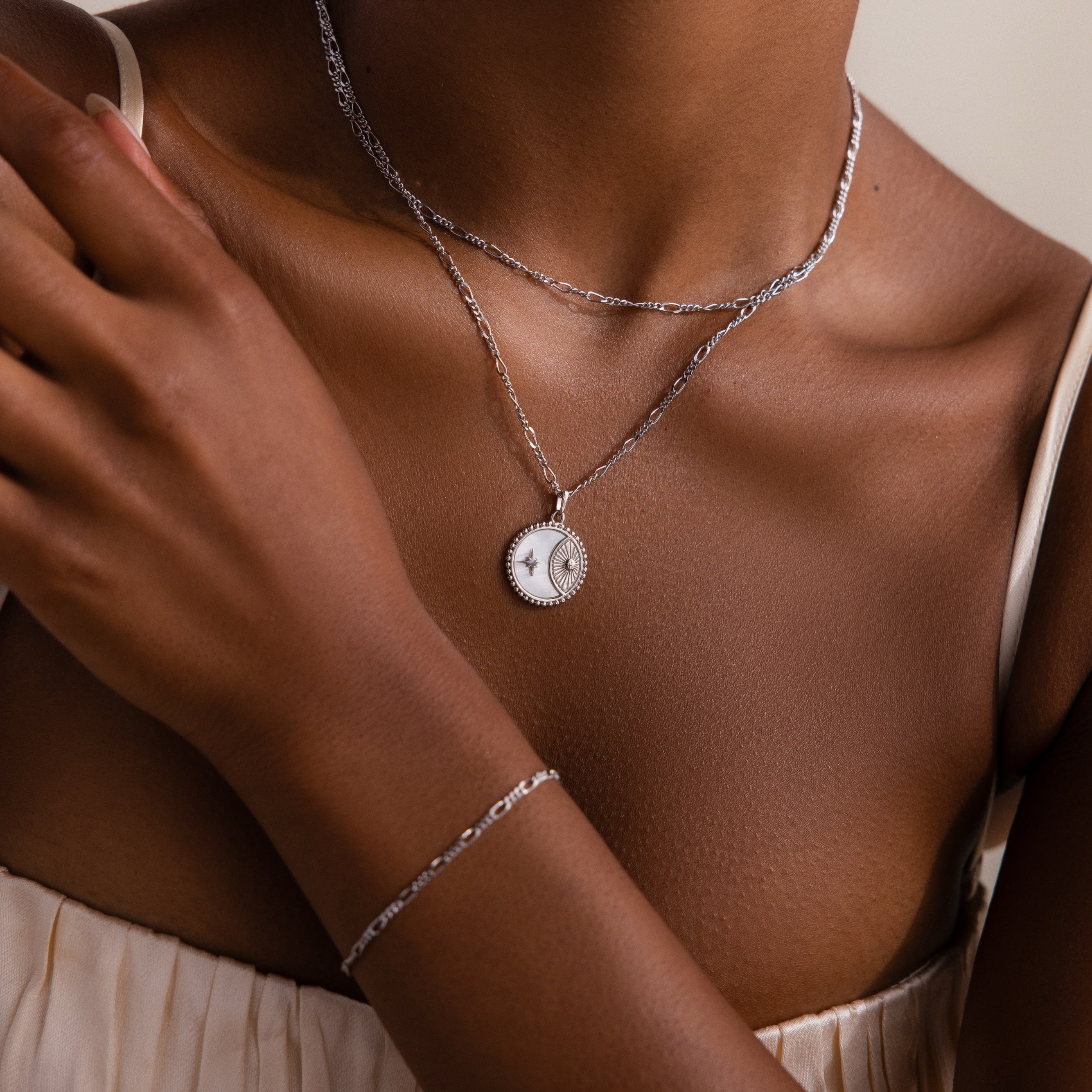A woman wearing layered silver necklaces, featuring the Gabi Coin Necklace with a sun and moon pendant, paired with a matching silver bracelet.