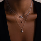 A person wears the Sun  Moon Eternity Necklace, layered with two other silver necklaces featuring unique pendants, against bare skin and a black top.