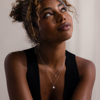A woman with curly hair wears the Laura Starburst Duo Necklace in Silver and a black sleeveless top, looking up against a neutral background.