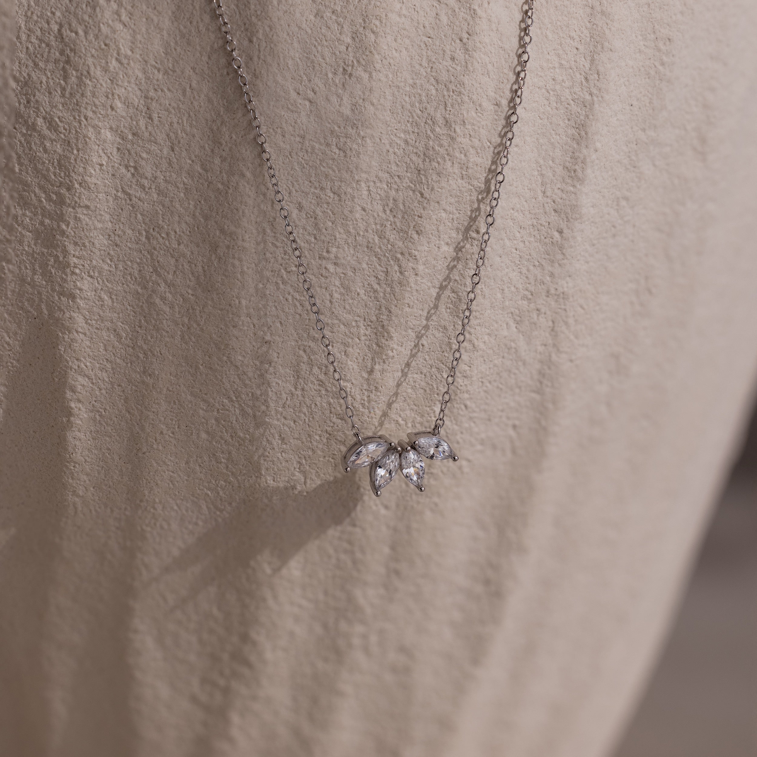The Marquise Diamond Necklace in Silver features three leaf-shaped gemstones, embodying the elegance of fine diamond jewelry against a light textured fabric.
