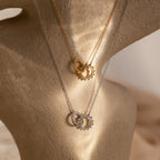 The Sun Moon Eternity Necklaces featured in gold and silver with sun and moon pendants, artfully intertwined and elegantly displayed on a textured stand.
