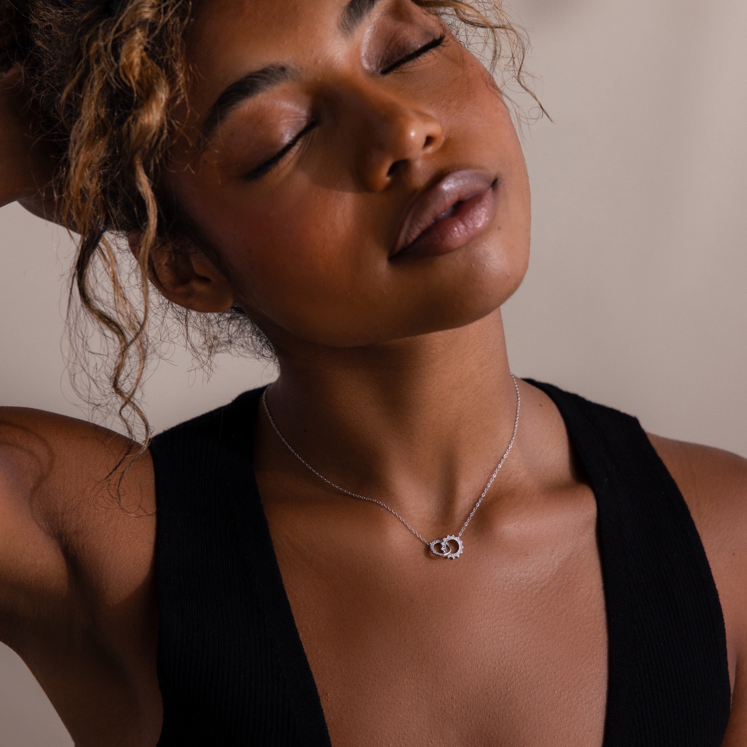A woman in a black top poses with closed eyes, showcasing the Sun  Moon Eternity Necklace with two interlocking silver circles.