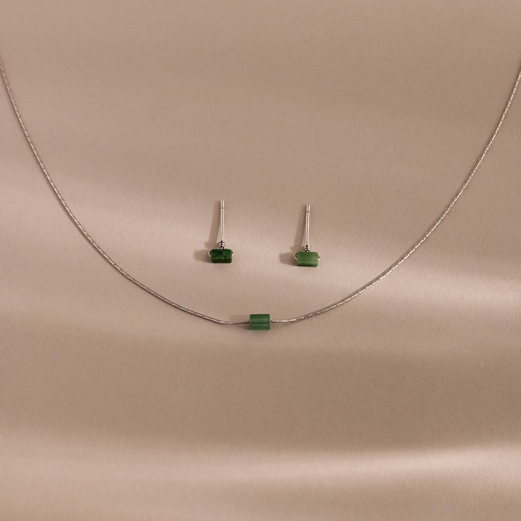 Jade Bar Jewelry Set in Sterling Silver, featuring a silver necklace with a small green bead and matching jade earrings, displayed on a beige background.