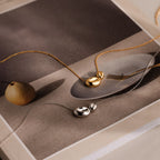 The Duo Pebble Necklace in Silver is displayed on an art book with a still-life image, adding elegant style to your jewelry collection.