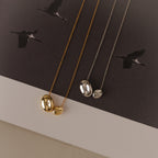 Two Duo Pebble Necklaces in gold and silver rest on paper with flying bird motifs, highlighting the necklaces elegant design and sense of freedom.