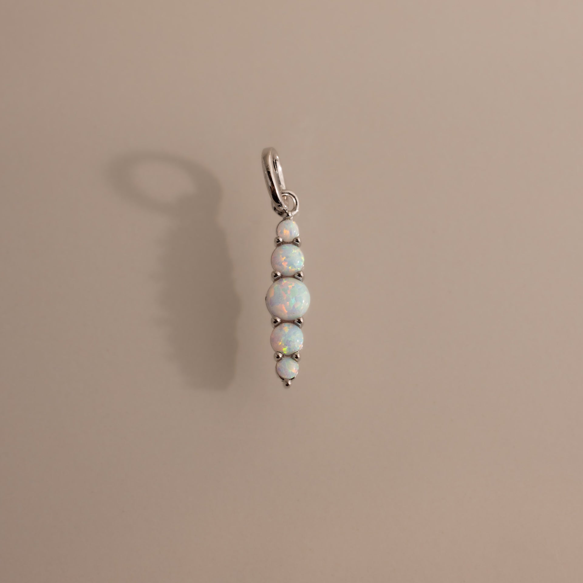The Ombre Lace Opal Charm features five round opal stones set vertically in silver, casting a soft shadow on beige—an ideal birth month gift.
