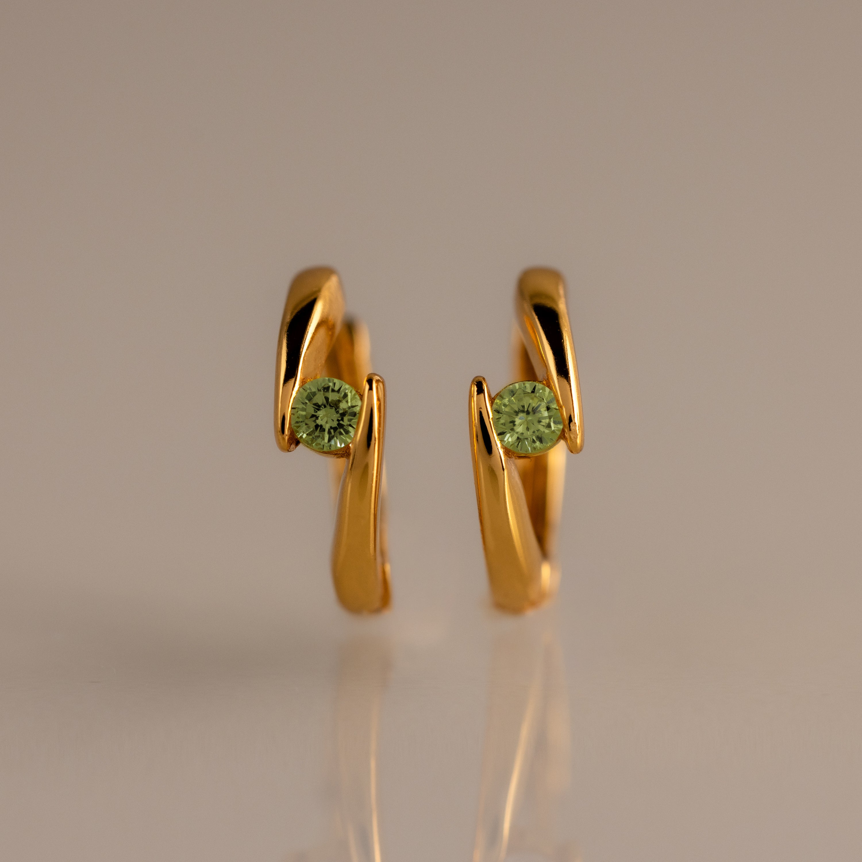 Floating Peridot Huggies—gold hoop earrings with green gemstones, personalized jewelry showcased upright on a neutral background.