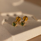 Peridot Flatback Studs with green gemstones, ideal as birthstone jewelry, are displayed on a textured, light-toned surface under warm lighting.