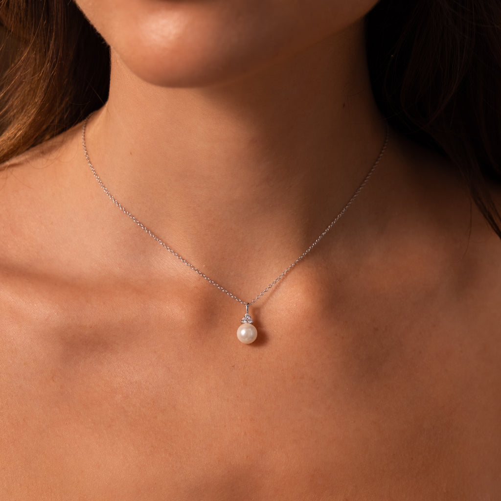 A woman displays timeless elegance wearing the Diamond Halo Pearl Necklace, featuring a single pearl pendant on her bare neck and shoulders.