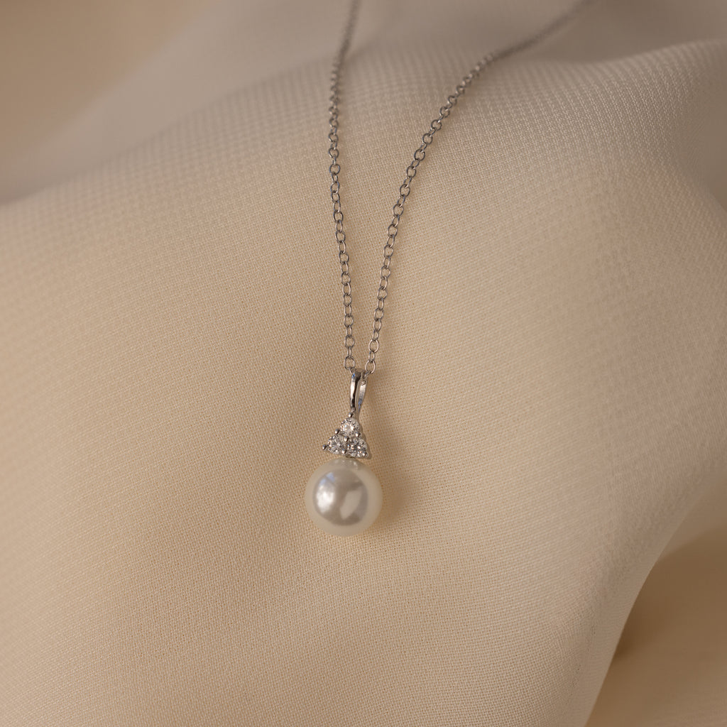 The Diamond Halo Pearl Necklace in Sterling Silver rests on soft, cream-colored fabric—a refined showcase of timeless elegance.