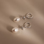 The North Star Pearl Hoops in Sterling Silver feature star accents and dangling pearls for a celestial look, shown on a beige background.