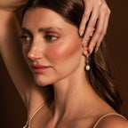 Woman with wavy brown hair wears North Star Pearl Hoops in Sterling Silver, touching her head with one hand.