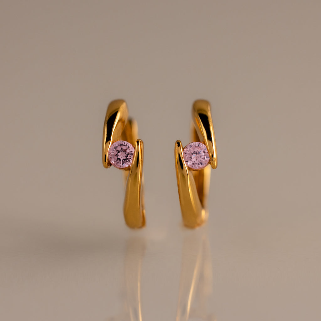 Floating Pink Tourmaline Huggies with a modern, curved design and pink gemstones are displayed on a neutral background.