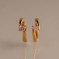 Floating Pink Tourmaline Huggies with a modern, curved design and pink gemstones are displayed on a neutral background.