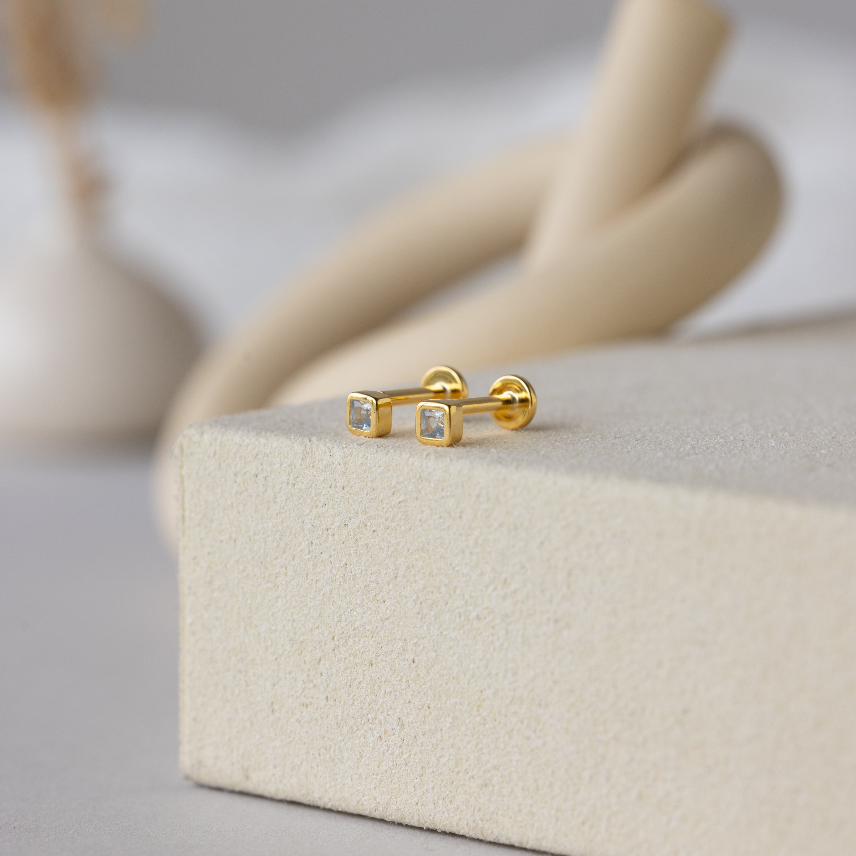 Square Bezel Aquamarine Flatback Studs are displayed on a light beige textured surface.