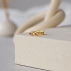 A pair of Square Bezel Birthstone Flatback Studs in Garnet (January), shown on a textured beige surface.