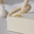 Square Bezel Diamond Flatback Studs with sparkling CZ gemstones are displayed on a textured beige surface.