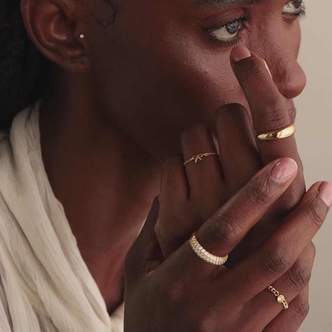 Close-up side profile of model showcasing a dainty gold bow ring on her middle finger, stacked with multiple gold rings.