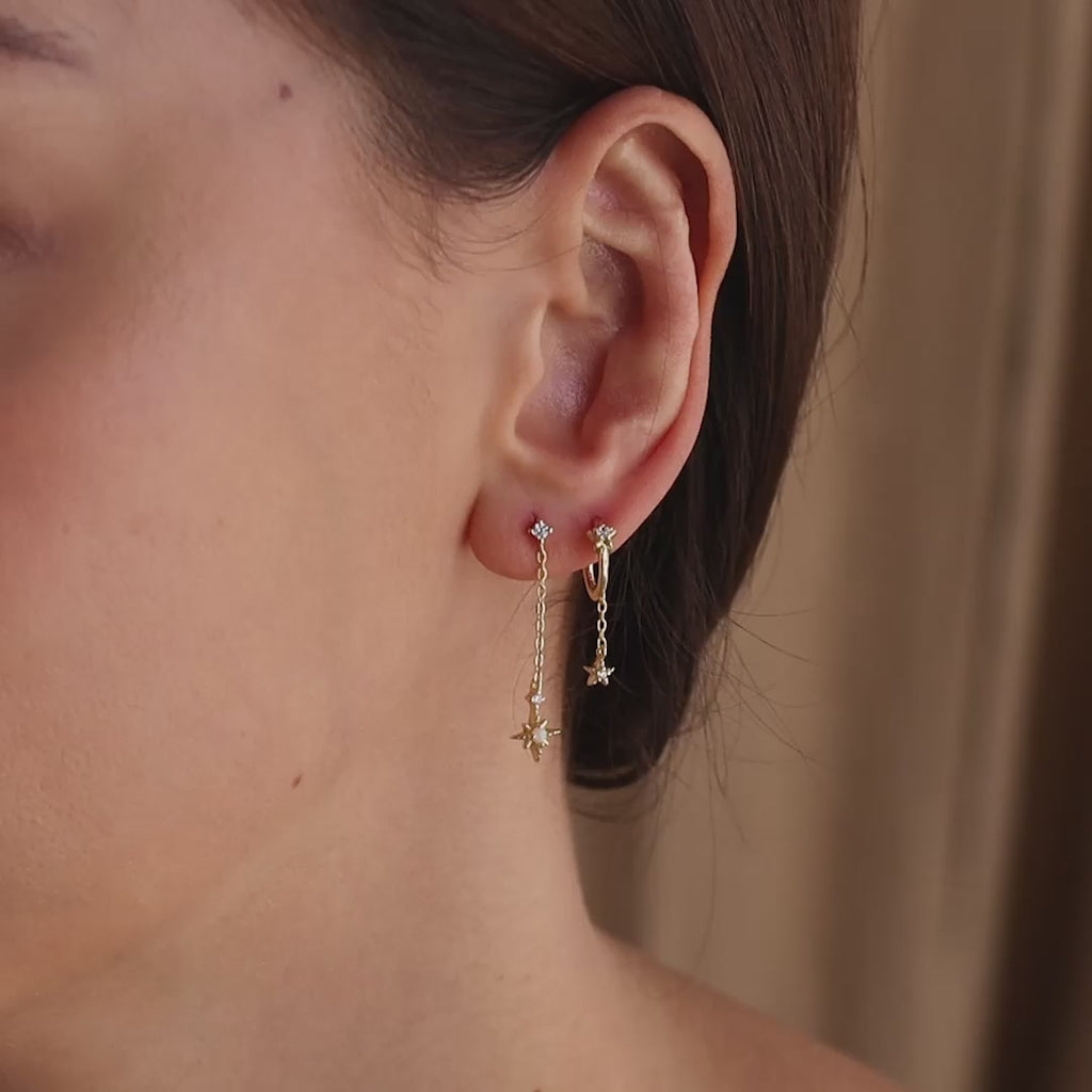 Model wearing a gold starburst chain stud earrings, accompanied by another star earring on a second piercing.