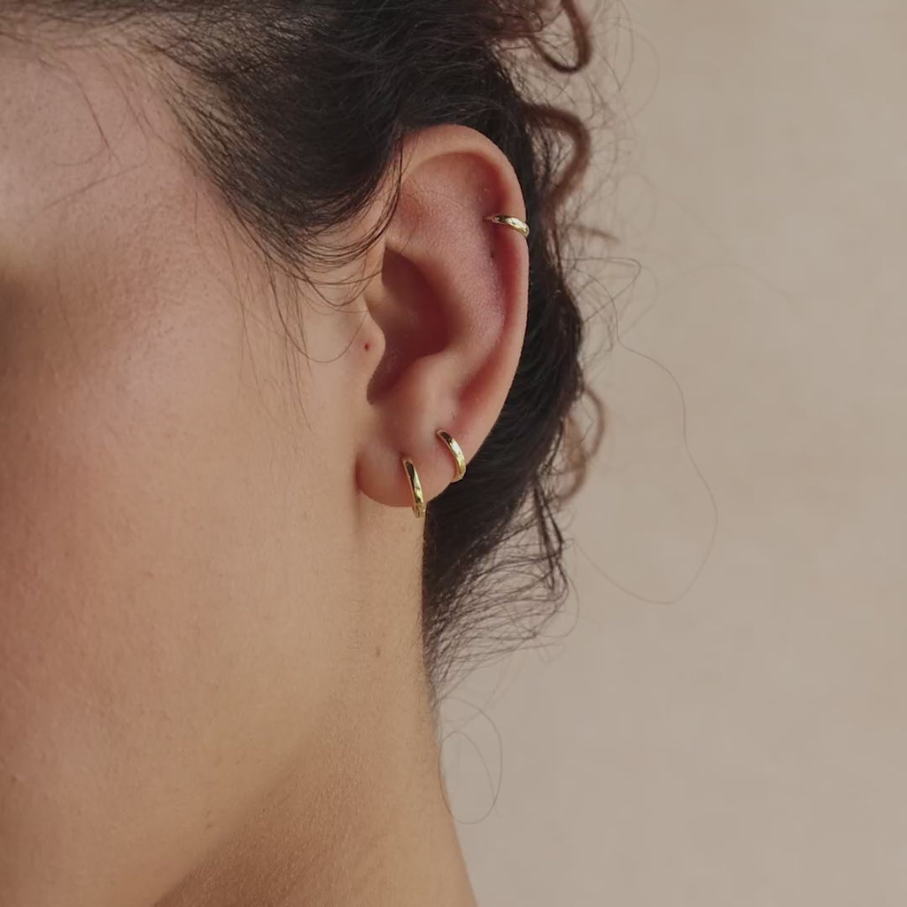 Close-up of model wearing three gold huggie hoop earrings in her helix and double lobe piercings.