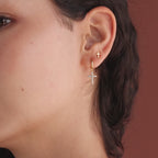 Model showcasing gold huggie hoop earrings with dangling pave cross charms, stacked with dainty cross stud earrings.