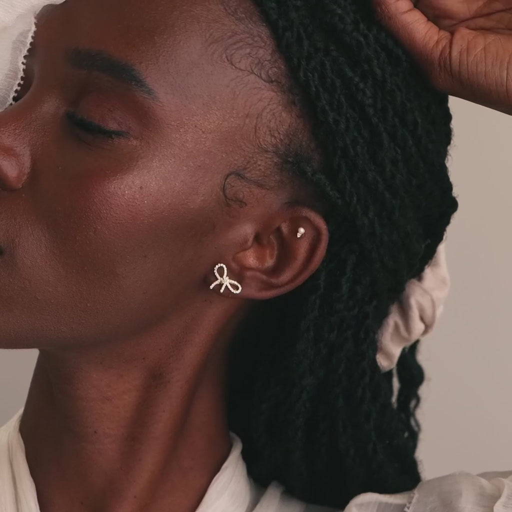 Model wearing gold pavé bow stud earrings paired with a dainty pearl and diamond stud earring.