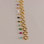 A full set of gold huggie earrings with baguette-cut birthstones arranged in a line, including garnet, sapphire, emerald, and more.