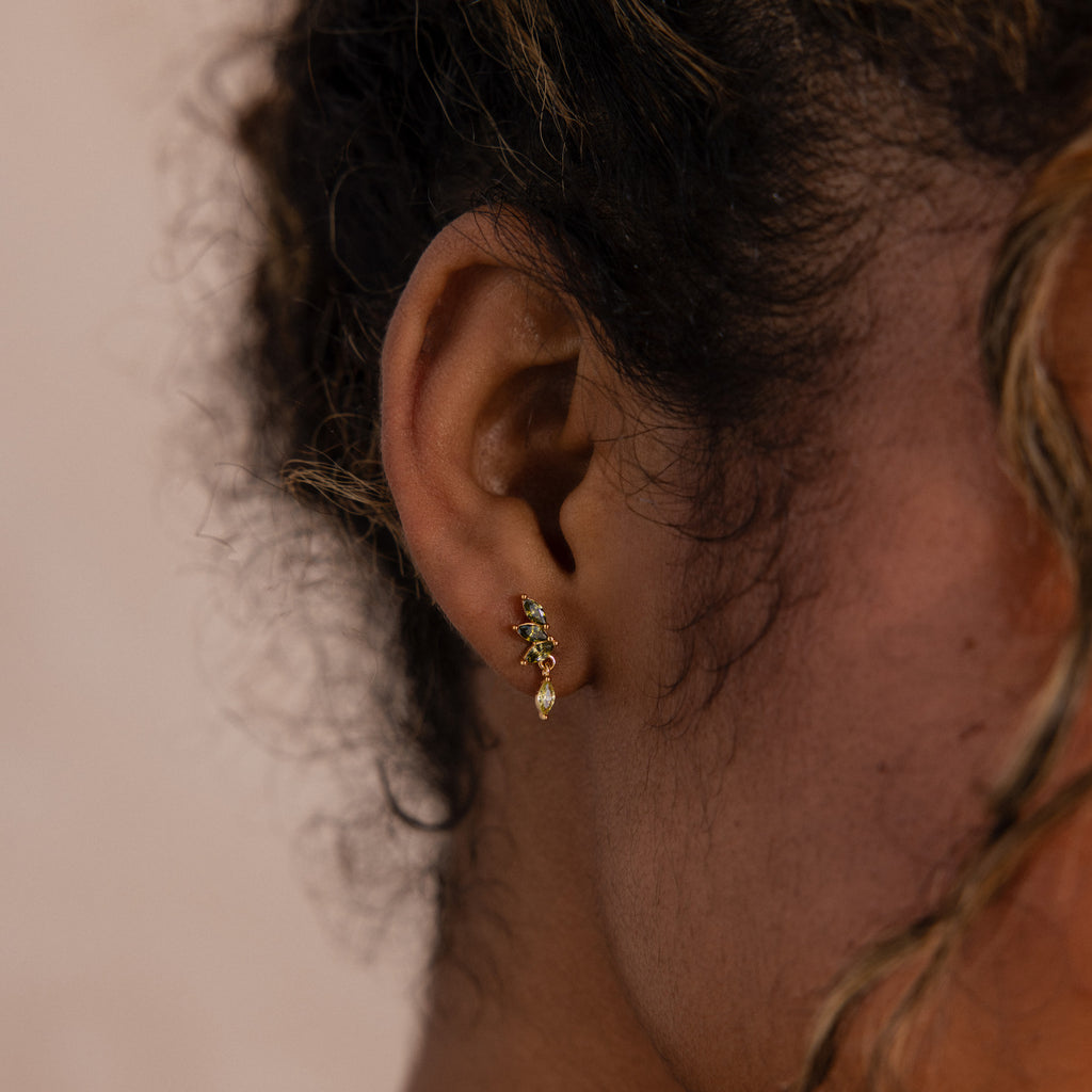 Model wearing gold marquise-cut drop earrings with green peridot gemstones arranged in a cascading leaf-inspired design.