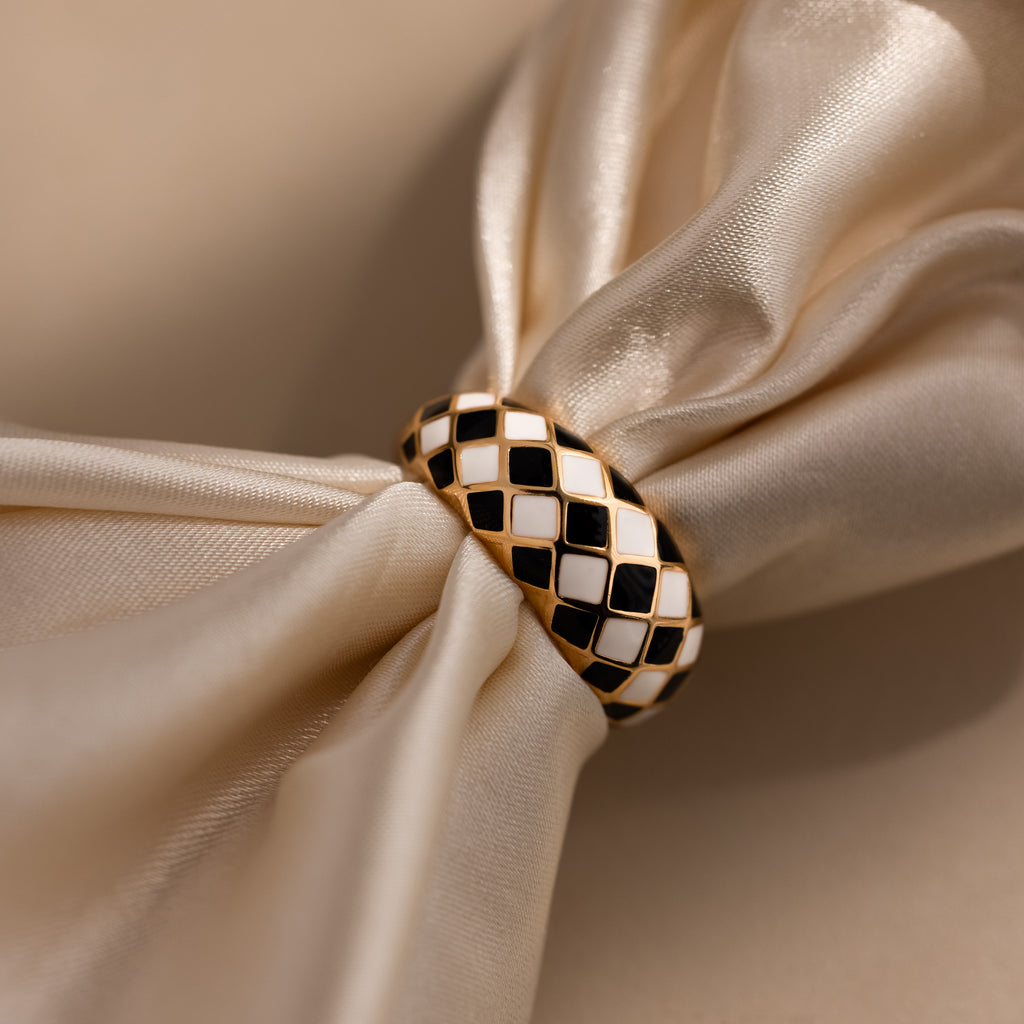 Gold dome ring with black and white checkered enamel pattern, displayed on a satin surface.
