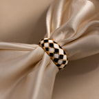 Gold dome ring with black and white checkered enamel pattern, displayed on a satin surface.