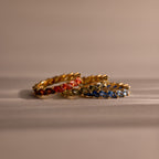 Set of gold rings with colorful red, green and blue stones on a beige surface