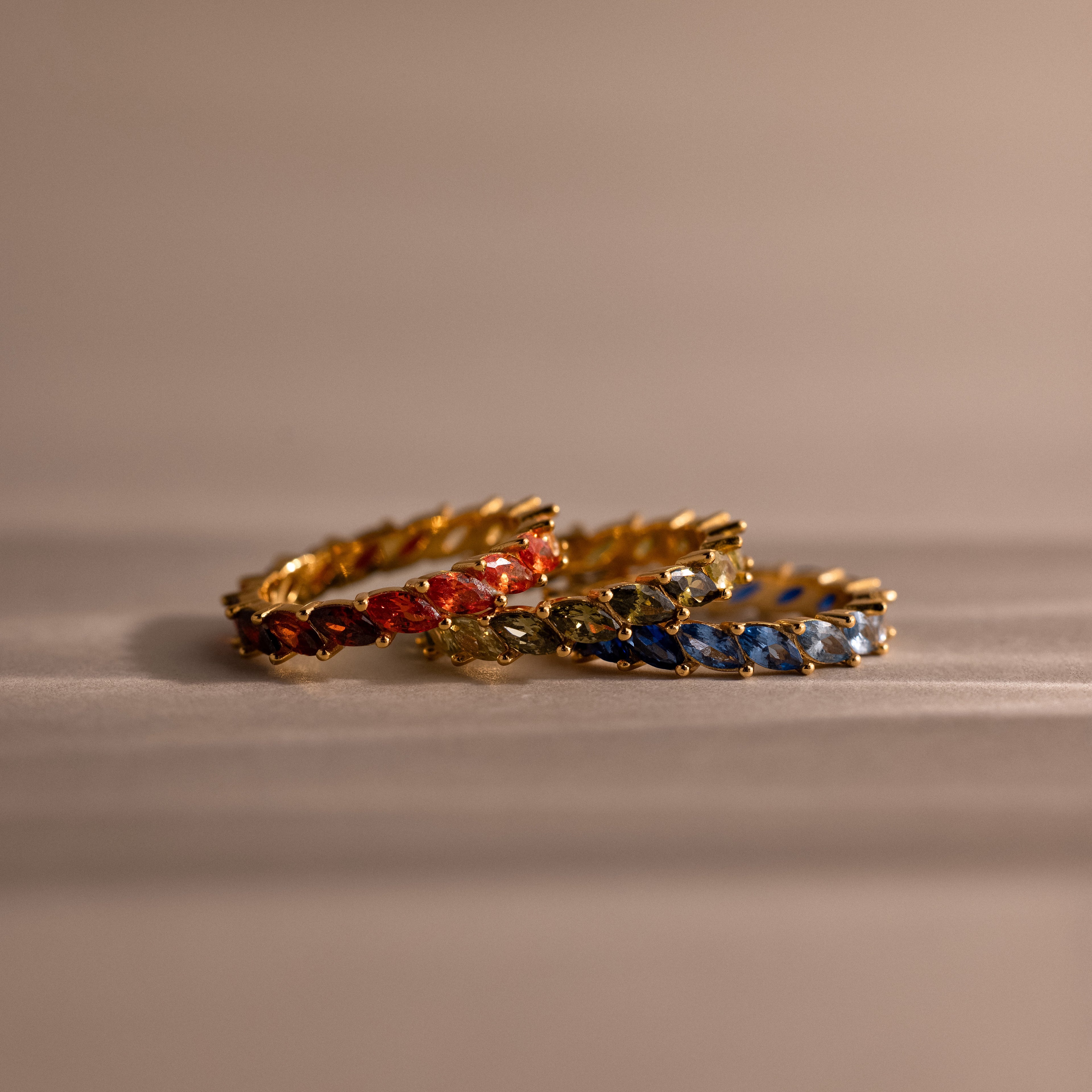 Set of gold rings with colorful red, green and blue stones on a beige surface