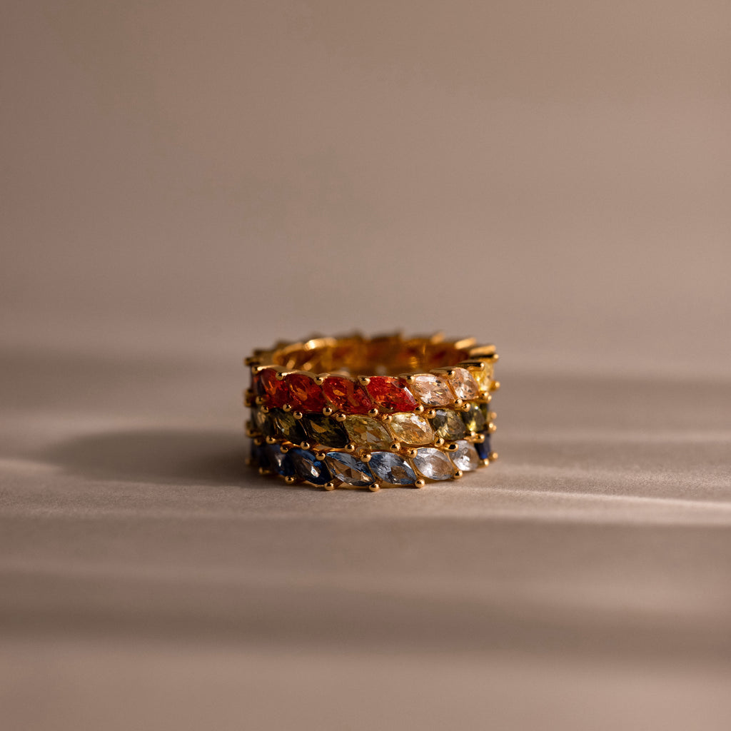 Gold rings with multicolored gemstones on a beige background