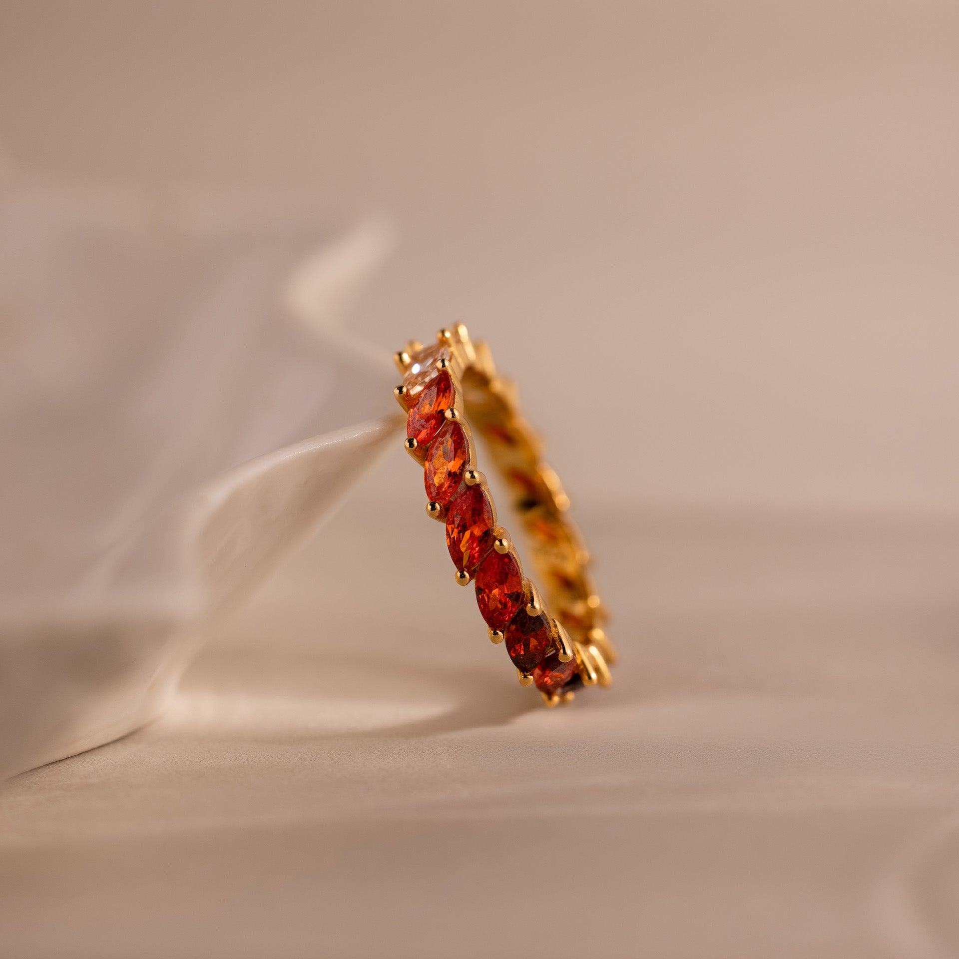 Red Marquise Ombre Ring with gradient marquise-cut stones in gold setting, resting sideways against a ceramic dish.