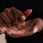 A gold ring with ombre red colored marquise stones held in a person's hand against a dark background