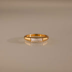 Diamond Baguette Signet Ring: This modern gold ring features a rectangular diamond centerpiece, showcased on a reflective beige surface.