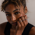 A woman with curly hair rests her chin on her hand, wearing the Duo Form Ring Set in Silver, as she gazes at the camera.