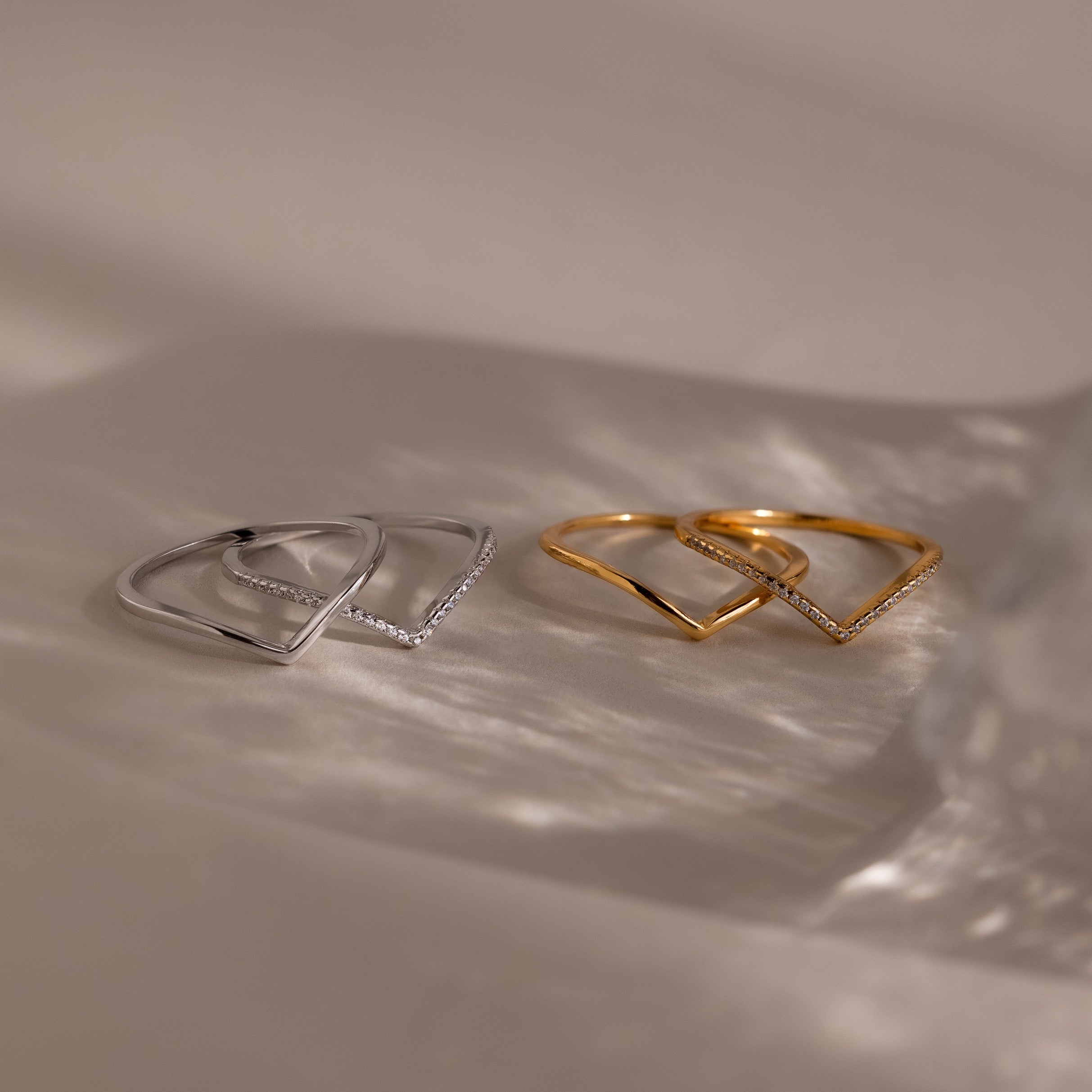 Four minimalist rings from the Curve Stacking Set, two in silver and two in gold, arranged on a neutral surface with soft shadows—ideal for a chic stacked look.