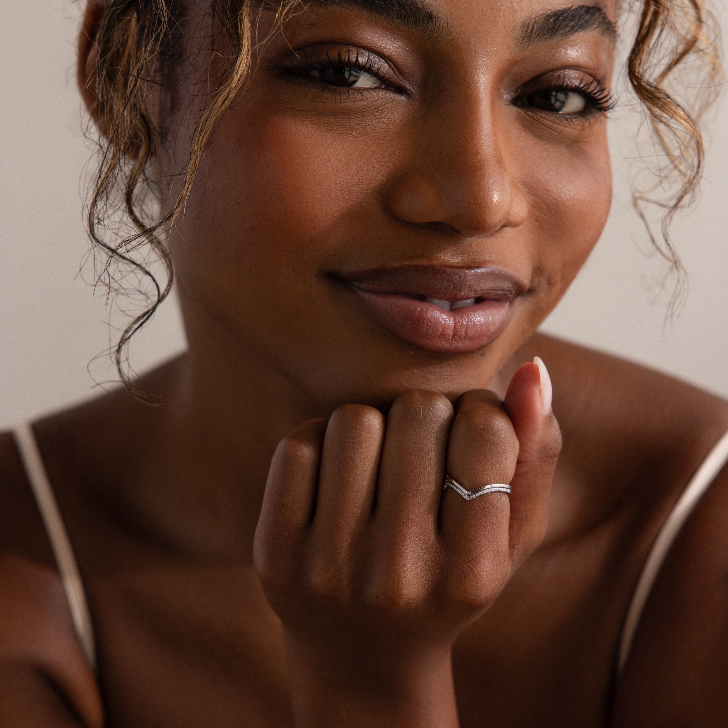 Woman smiling softly, resting her chin on her hand, wearing a white top and the Curve Stacking Set in Silver—delicate thin bands that add subtle elegance to her look.