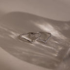 The Curve Stacking Set in Silver features two delicate rings with angular designs, ideal for a modern stack and shown casting soft shadows on a neutral background.