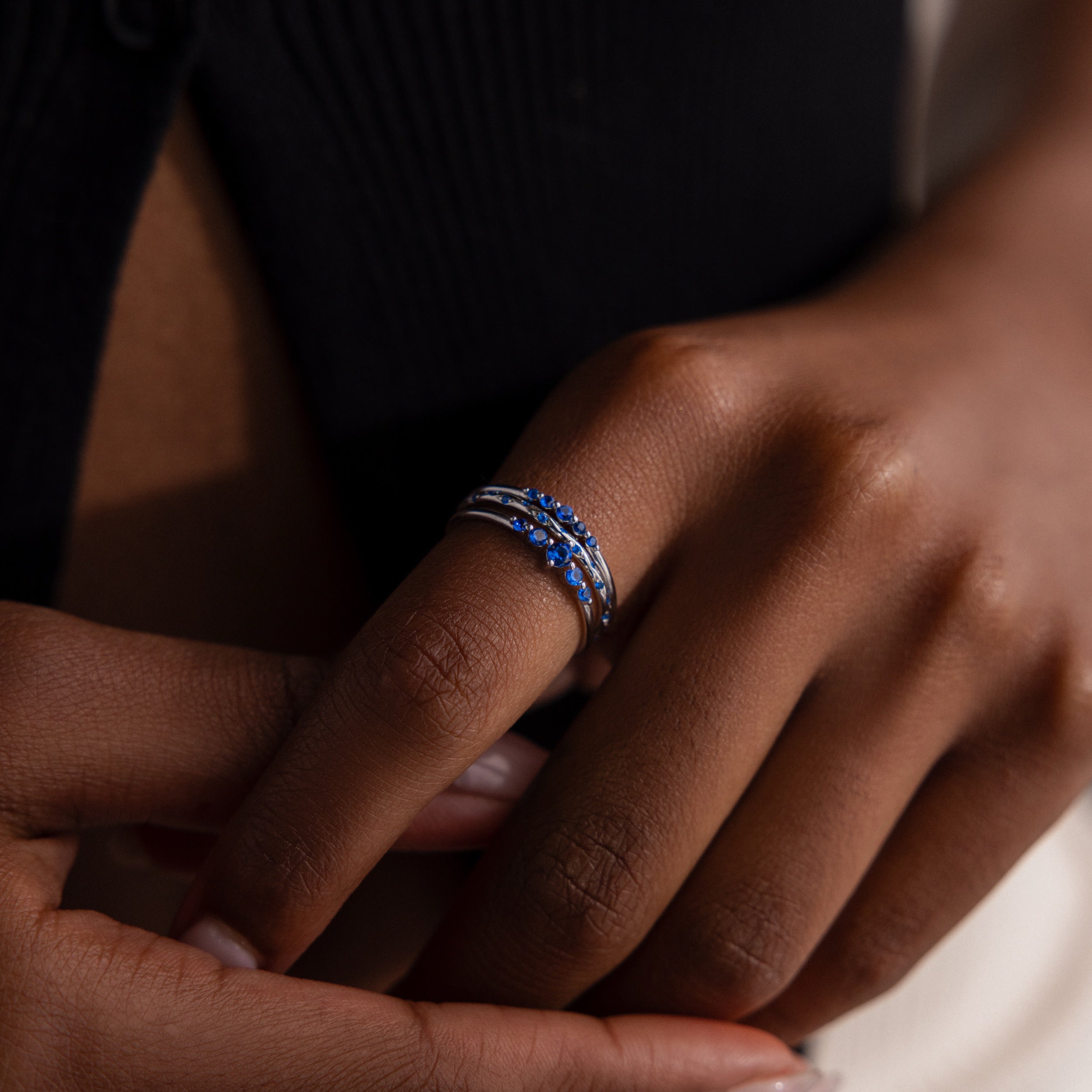 Close-up of a model wearing a stack of silver rings with blue gemstones.