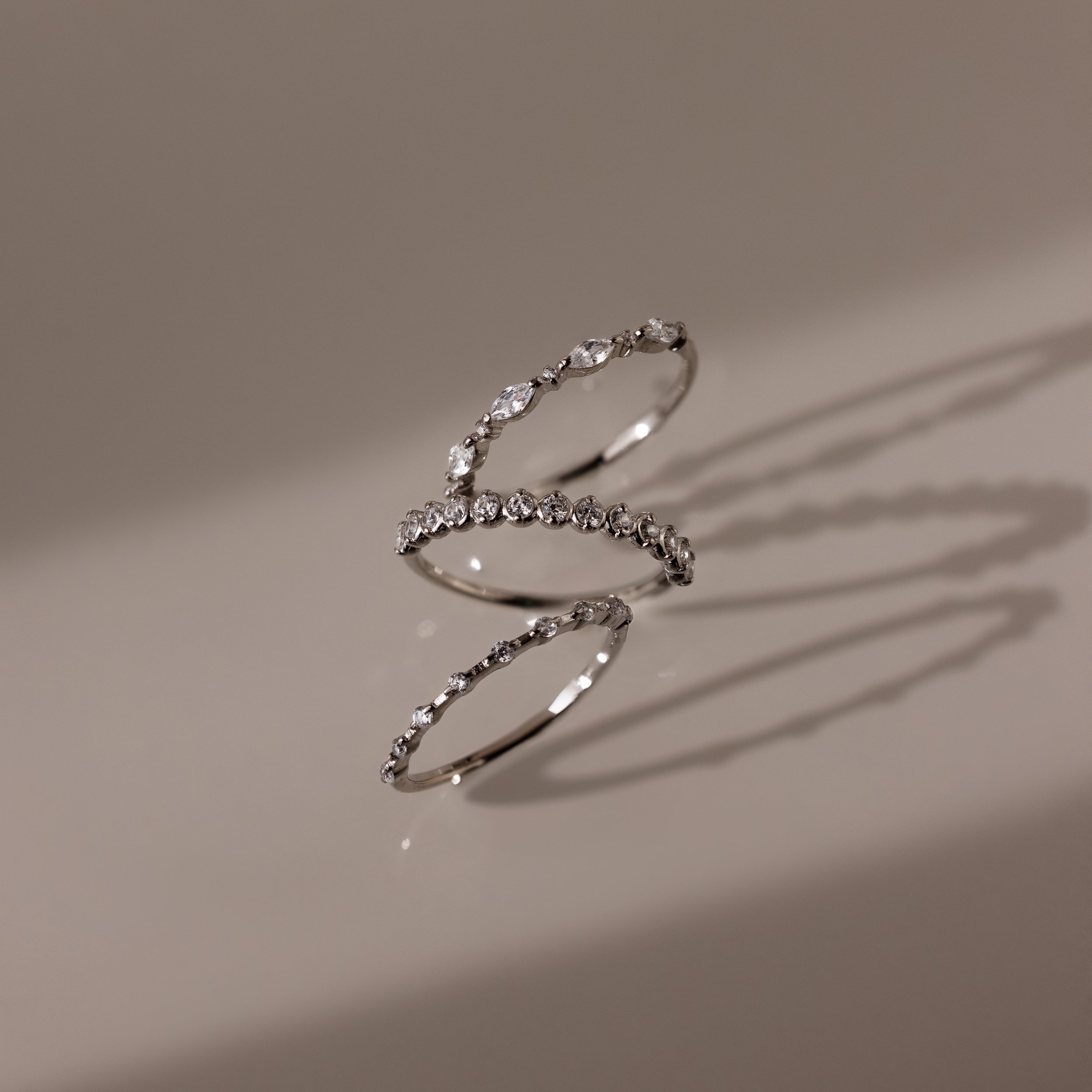 The Crystal Stacking Ring Set in Silver rests on a beige surface, each ring casting soft shadows as their gemstones sparkle delicately.