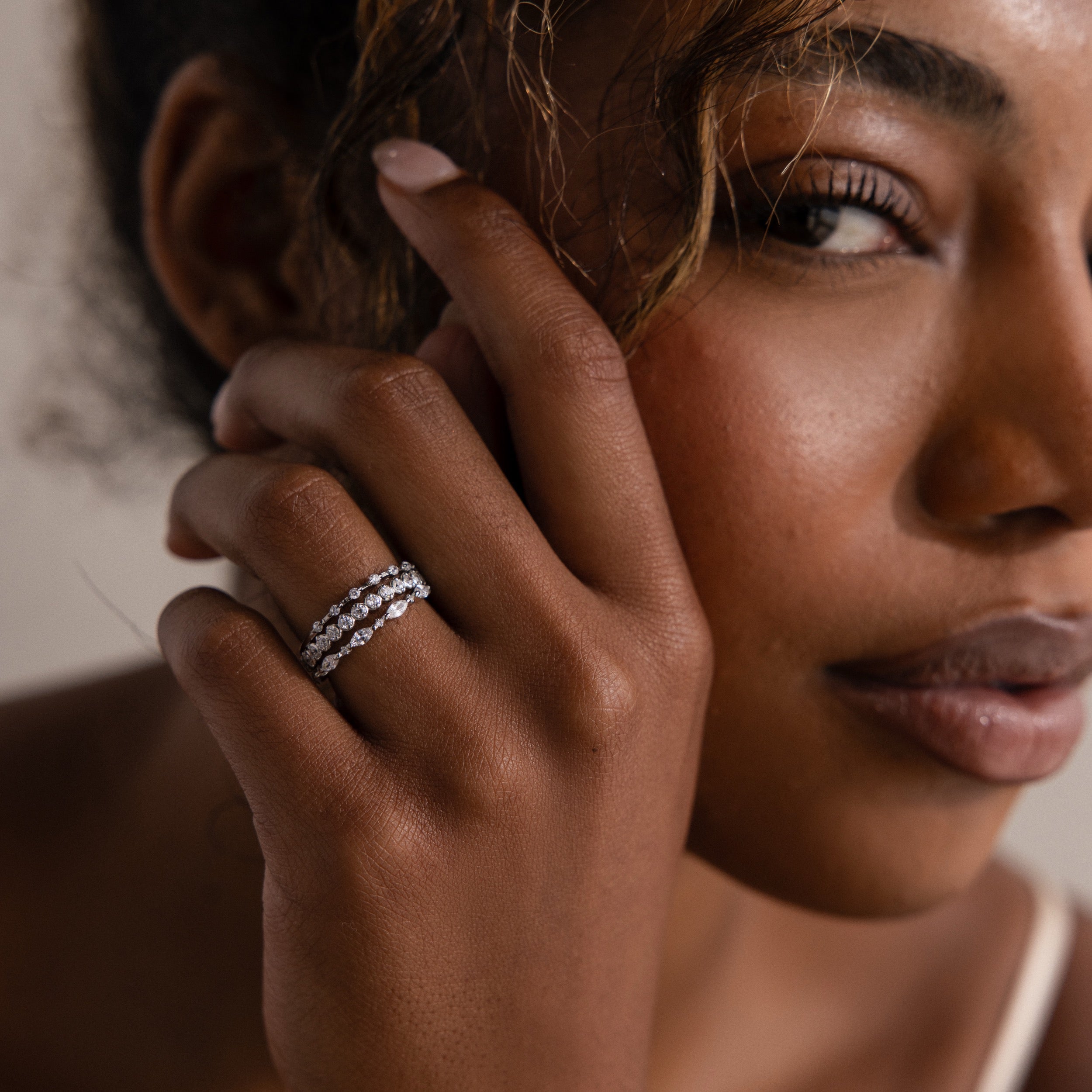 Elegant woman with curly hair showcases the Crystal Stacking Ring Set in Silver, adorned with sparkling gemstones, as she gazes softly at the camera.