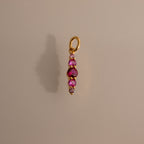 The Ombre Lace Ruby Charm is a gold pendant with four pink gemstones set vertically on a plain background.