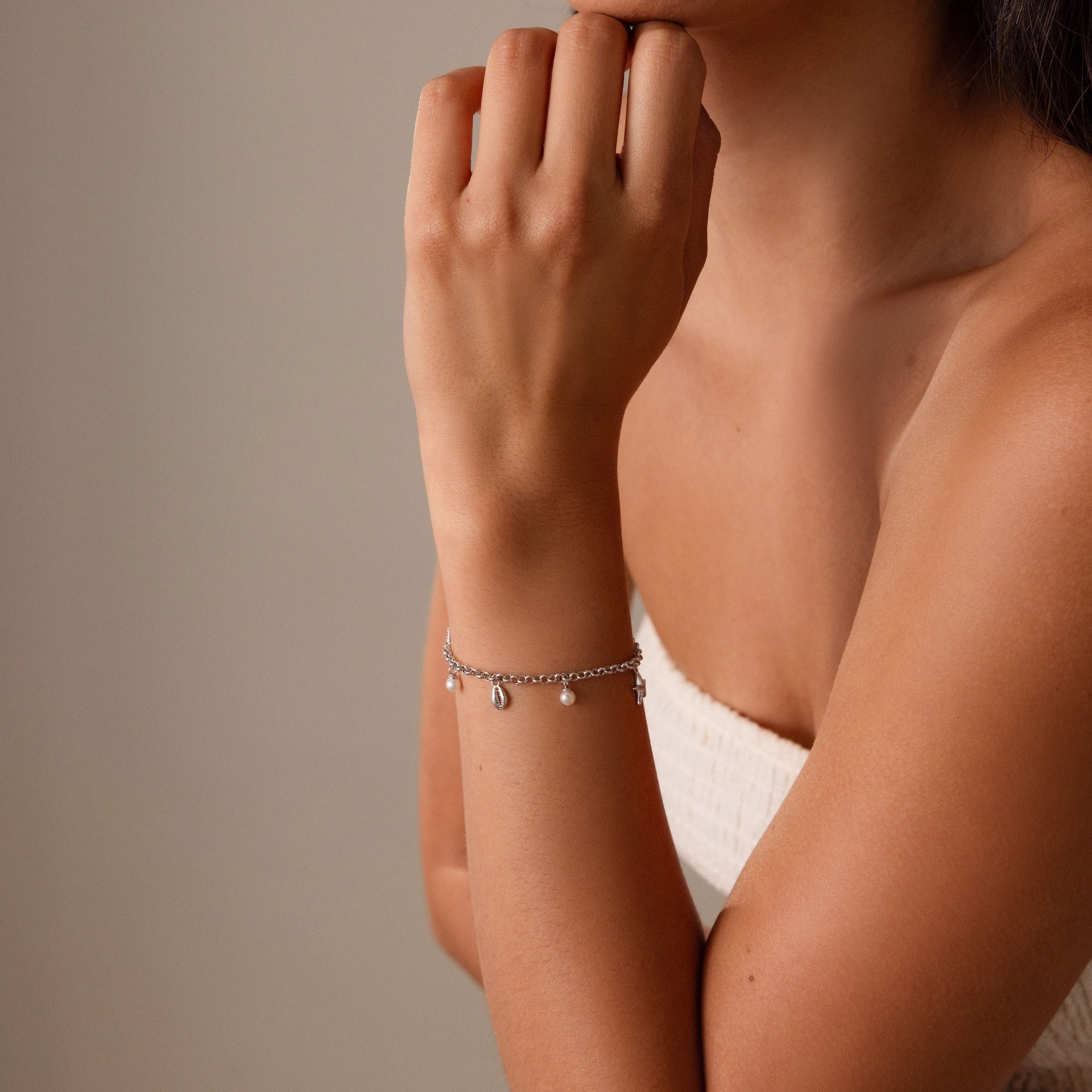 Woman wearing a Seaside Pearl Charm Bracelet in Silver and a white top poses with her hand near her chin, highlighting the elegant coastal jewelry.