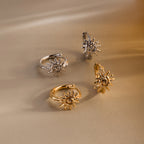 Two pairs of Celestial Sun Huggies—gold and silver—gleam as statement jewelry on a beige surface under warm light.