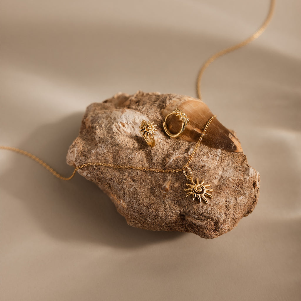 Celestial Sun Huggies earrings shine on a textured rock under soft lighting, creating a striking statement jewelry look.