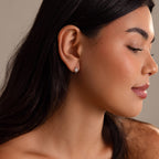 Woman with long dark hair, eyes closed, facing right, wears Celestial Sun Huggies—small, sparkling earrings for an elegant statement.